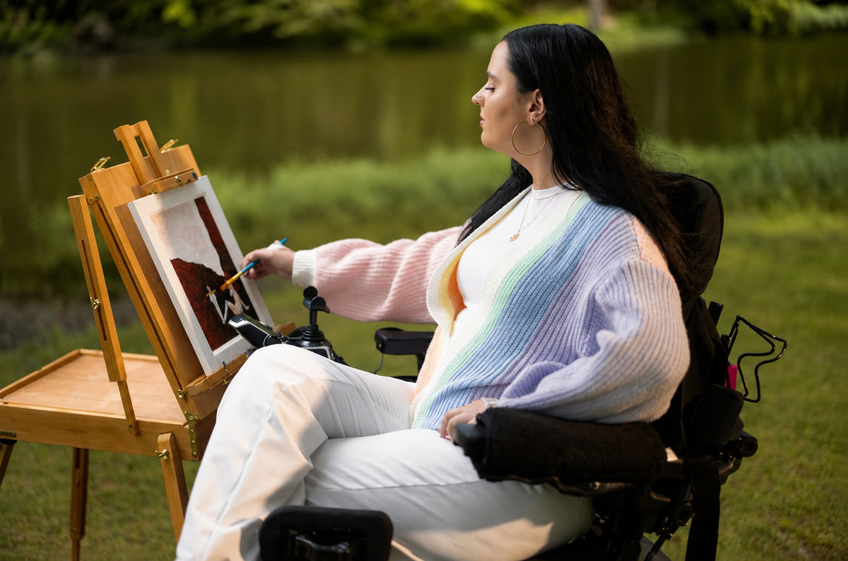 Woman in a wheelchair painting outdoors on an easel